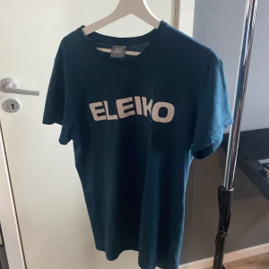 Blå Eleiko t-shirt i bomull - Säljer en blå t-shirt från Eleiko i storlek L. T-shirten har klassisk passform, rund hals och korta ärmar. Stor vit Eleiko-logga framtill. Skön och enkel modell i mjuk bomull, perfekt för gymmet eller chill dagar.
