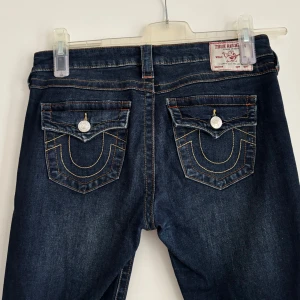 True Religion mörkblå bootcut jeans - Mörkblå jeans från True Religion. Dem är låg midjade och bootcut. I storlek W29 och i modellen ”Joey”. Midjemått rakt över: 39 cm ( X2=78 cm ). Innerbenslängden: 78 cm. Säljer även 2 par andra trueys just nu på min sida. Skriv om du har frågor💗