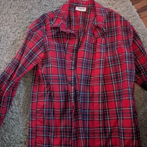 Röd rutig skjorta från KappAhl stl 146 - Röd långärmad skjorta från KappAhl med klassiskt rutigt mönster i svart och vitt. Skjortan har knappar framtill och en avslappnad passform, perfekt att bära öppen eller stängd. Tillverkad i mjuk bomull för en skön känsla.