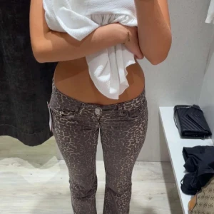 Leopardmönstrade lågmidjade jeans - Säljer ett par snygga lågmidjade jeans med leopardmönster. Byxorna har klassisk femficksdesign, knapp och dragkedja framtill samt raka ben. Perfekta för dig som vill sticka ut med ett djurmönster och gillar en trendig look.