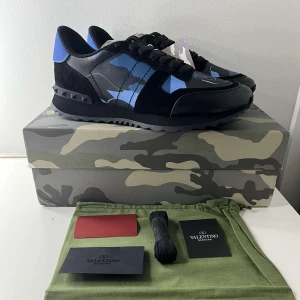 Valentino Rockrunner  -  Valentino Rockrunner sneakers i svart och blått med kamouflagemönster. Skorna har svarta mockadetaljer och svarta snören. Extra snören, box, tags och en påse tillkommer i köpet. 