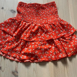  Kjol från Zara - Supersöt röd kortkjol med små vita blommor och volangdetaljer. Kjolen har smock i midjan för en bekväm passform och är perfekt för varma dagar. Lätt och luftig känsla, passar perfekt till sneakers eller sandaler.