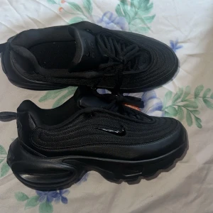 Svarta Nike Air Max sneakers - Säljer ett par helsvarta Nike Air Max sneakers med chunky sula och klassisk Air-dämpning. Skorna har mesh och syntet på ovandelen, snörning och diskret Swoosh-logga på sidan. Perfekta för dig som gillar en sportig och clean look.