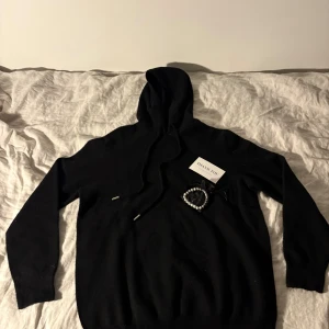 Grisch Svart Hoodie - Helt ny. Mysig svart hoodie i kashmir med huva och dragsko. Tröjan har lång ärm och en klassisk, enkel design som passar perfekt till lager-på-lager. Snygg och stilren för dig som gillar en clean look.
