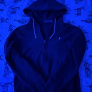 Polo Ralph Lauren - Säljer en väldigt fin, äkta marinblå Ralph Lauren kofta med vit logga. I väldigt fint skick inga fläckar eller hål någonstans. Helt äkta (finns QR kod på etiketten). Det är en liten M men passar stor S också. 175cm max. Säljer för att jag har vuxit ur den nu :)