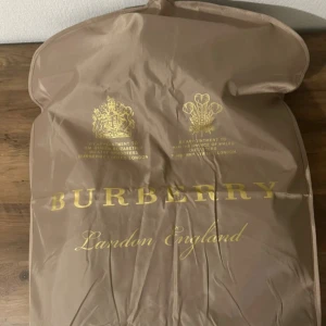 Svart pufferjacka från Burberry  - Säljer en svart pufferjacka från Burberry med klassisk rutig grå, vit och röd insida på huvan. Jackan har dragkedja framtill, huva och Burberry-logga på ärmen. Perfekt för kalla dagar och har en riktigt snygg, modern look.Storlet M men passar som S