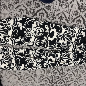 Svarta och vita mönstrade byxor - Säljer ett par svarta och vita byxor med ett unikt blommigt och abstrakt mönster. Byxorna har en loose passform och är tillverkade i ett mjukt bomullsmaterial som känns skönt mot huden. Perfekta för dig som gillar att sticka ut med din stil.