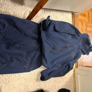 Nike tech  marinblå och grå/svart byxorna är xl och flisarna är xxl - Två snygga Nike tech tracksuits  med dragkedja och huva. En är marinblå med svarta detaljer och hel dragkedja, den andra är grå och svart med neongul Nike-logga. Båda har långa ärmar och är perfekta för chill eller träning. Materialet är mjuk bomullsmix.