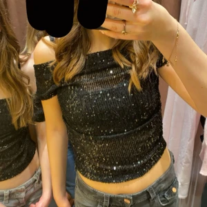 Svart paljettopp från Gina Tricot - Säljer en svart croppad topp från Gina Tricot med paljetter över hela. Toppen har offshoulder-modell, perfekt för att sticka ut. Materialet är glittrigt, Den har ett litet linne inbyggt så den är inte genomskinlig,perfekt till nyår! Eller än fest 