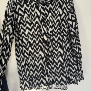 Svartvit mönstrad skjorta - Säljer en svartvit skjorta med coolt zigzag-mönster. Skjortan har långa ärmar och knappar framtill. 