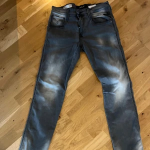 Replay Anbass grå jeans, stl 29 - Snygga Replay Anbass jeans i grå tvätt med slitningar och klassiska fem fickor. Jeansen har smal passform och dragkedja i gylfen. Perfekta för dig som gillar en modern och stilren look. Materialet är mjukt och stretchigt för extra komfort.