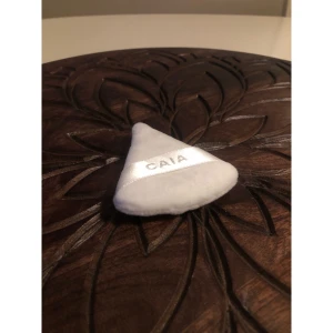 Vit beautyblender från CAIA - Supermjuk, vit triangelformad beautyblender (puff) från CAIA med ett band i satin där märket står tryckt. Perfekt för att applicera puder eller fixa basen. Materialet är fluffigt och känns lyxigt mot huden.
