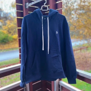 Marinblå hoodie från Polo Ralph Lauren - I princip helt ny. Snygg marinblå hoodie från Polo Ralph Lauren med vit snörning och klassisk logga på bröstet. Tröjan har huva, känguruficka och ribbade muddar. Perfekt för chill dagar och enkel att matcha med jeans eller joggers.