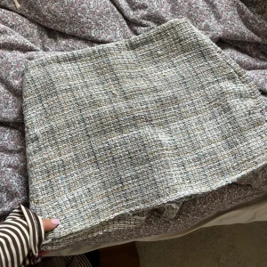 Tweed kortkjol från Zara i grått - Säljer en snygg kortkjol från Zara i tweed med grå, beige och blå toner. Kjolen har en rak passform och är tillverkad i ett grovt vävt material som ger en exklusiv känsla. Perfekt att styla med boots eller en stickad tröja.