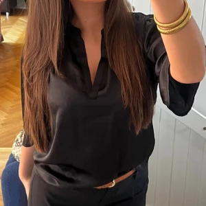 Svart sidenblus med v-ringning - Säljer en svart blus i glansigt sidenmaterial med v-ringad hals och trekvartsärm. Blusen har en avslappnad passform och är perfekt för dig som gillar stilrena och eleganta plagg. Snygg att styla med jeans eller kostymbyxor.