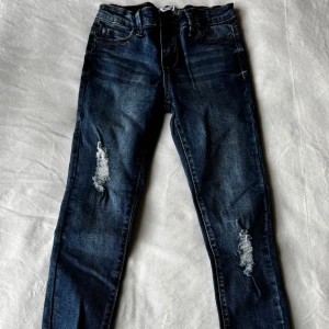 Blå jeans med slitna detaljer - Blå jeans från Denim Day i storlek 140. Slitna detaljer på benen. Fraktar inom 24h!