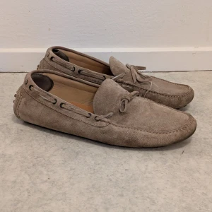 Brunello Cucinelli, Mockaskor, beige – stl 44 (Carshoe) - Brunello Cucinelli, (Laced Carshoe), Beige Suede, stl 44. Säljer dessa exklusiva Brunello Cucinelli Carshoe i äkta mocka, storlek 44. Skorna är begagnade och behöver kärlek:  Ytan är lätt smutsig, snöret är trasigt/trådsläpp (se bild). Innermått ca 29 cm. Perfekt för den som vill ha ett par Cucinelli till fyndpris och är beredd att fixa snörena! Nypris 7199 kr