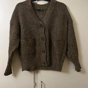 Brun stickad kofta från 157 - Mysig brun stickad kofta i toppskick från 157 med grov ribbad struktur, djup v-ringning och stora framfickor. 