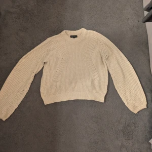 Beige stickad tröja  - Säljer en beige stickad tröja från med snyggt hålmönster på framsidan och ärmarna. Tröjan har rund hals, ribbade muddar och är lite croppad i modellen. 