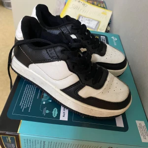 Svarta och vita sneakers 157 Archie Star - Säljer ett par snygga sneakers från 157 i modellen Archie Star. Skorna är svartvita med cool kontrast mellan färgerna, har snörning och en klassisk rund tå. Ovandelen är i syntetmaterial och de har en platt sula som passar till många outfits.