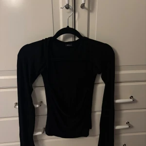 Svart långärmad topp  - Säljer en svart långärmad topp. Toppen har en tight passform och är tillverkad i mjukt material som känns skönt mot huden. Den har en stilren, minimalistisk look med raka linjer och passar perfekt till jeans eller kjol.