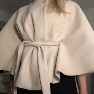 Beige Poncho - Trendiga poncho Blair från missäy i en snygg beige färg. Den har snöre i midjan samt knapp upptill. Den perfekta kappan för att få outfitsen att se extra snygga ut!! Knappt använd och i nytt skick