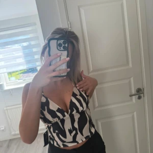 Zebramönstrad croppad linnetopp - Säljer en snygg croppad linnetopp med zebramönster i svart och vit. Toppen har smala axelband och en djup v-ringning framtill som ger en trendig look. Perfekt för dig som vill sticka ut med ett coolt mönster och fräsch stil.