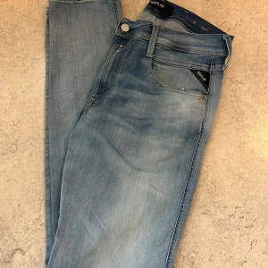 Ljusblå Replay Anbass jeans - Säljer ett par helt nya ljusblåa Replay Anbass jeans i storlek 32/32. Jeansen har en slim passform med klassisk femficksdesign och snygga detaljer vid fickorna. Tillverkade i stretchigt jeansmaterial för extra komfort. Perfekta för dig som gillar en modern och stilren look.