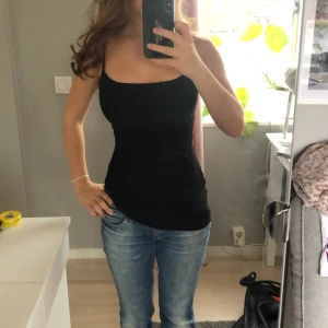 Svart tight linnetopp med smala axelband - Säljer en svart, figurnära linnetopp med smala axelband och rak urringning. Toppen är enkel och stilren, perfekt att matcha med jeans eller kjol. Materialet känns mjukt och stretchigt för en bekväm passform🥰