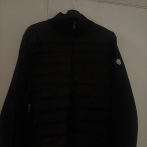 Svart dunjacka från Moncler Strolek M - Svart hybrid cardigan från Moncler med quiltad front och klassisk logga på ärmen. Jackan har dragkedja framtill och är tillverkad i en mix av dun och polyester. Perfekt för dig som vill ha en stilren och varm jacka med exklusiv känsla.                      - kan gå ner i pris vid snabb affär  - Finns i Göteborg  - Kan även fraktas