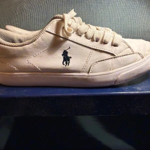 Vita sneakers från Polo Ralph Lauren - Fräscha vita sneakers från Polo Ralph Lauren med klassisk låg profil och rund tå. Skorna har snörning, mjuk textil på insidan och är tillverkade i skinn med Polo-logga broderad på sidan. Snyggt stilrena och passar perfekt till jeans eller shorts. 