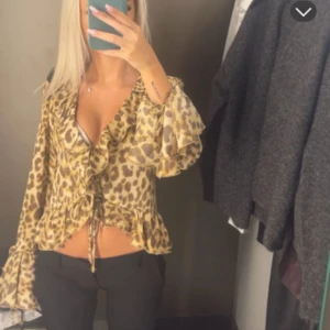 Leopardmönstrad blus med volanger - Säljer en snygg blus med leopardmönster och volangdetaljer. Blusen har djup v-ringning, snörning i midjan och vida långa ärmar med volang vid ärmslut och nederkant. Perfekt för dig som vill sticka ut med en trendig look.