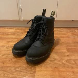Dr. Martens boots i skinn - Knappt använda Klassiska svarta Dr. Martens boots med snörning och grov sula. Vattentäta! Skorna har rund tå, gula sömmar och dragflik med logga baktill. Tillverkade i skinn och syntet, perfekta för dig som vill ha en tidlös stil. 