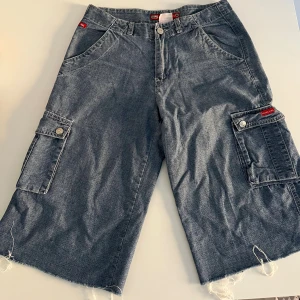 Blåa jeans cargoshorts från Moda Lisa - Säljer ett par blå jeans cargoshorts från Moda Lisa. De har flera stora fickor med knappar på sidorna och bak, samt råa, fransiga benslut. Sitter mer som S än M. Passar dig här strl 25 i midjan.