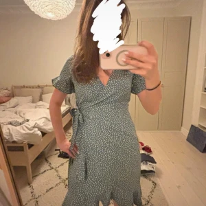 Prickig omlottklänning från Vero Moda - Supersöt blå omlottklänning från Vero Moda med vita prickar, korta ärmar och knyt i midjan. Klänningen har v-ringning och volangdetalj nertill. Perfekt för sommarens alla tillfällen!