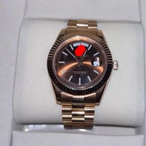  Day Date herrklocka - Säljer en lyxig guldfärgad Day-Date med svart urtavla och dag- samt datumvisning. Klockan har en klassisk rund form, räfflad bezel och länkarmband i metall. Perfekt accessoar för dig som gillar exklusiv stil och tidlös design.