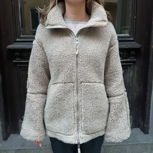 Beige teddyjacka med dragkedja - Intresekoll på min Mysig beige teddyjacka med hög krage och hel dragkedja framtill. Jackan har två stora fickor och en avslappnad passform. Perfekt för kyliga dagar när du vill vara både varm och snygg. Tryck inte på köp nu utan skriv till mig om ni är intresserade❤️