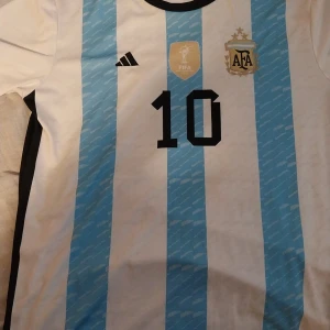 Argentina Messi #10 fotbollströja Adidas - Säljer en officiell Argentina fotbollströja från Adidas med Messi och nummer 10 på ryggen. Tröjan har klassiska ljusblå och vita ränder, svart krage och detaljer i guld. Tillverkad i återvunnen polyester, perfekt för dig som älskar fotboll och Messi.den är typ använd bara 4gånger.kan frakta 