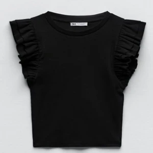 Svart topp med volangärmar från Zara - Svart topp från Zara med rund halsringning och volangdetaljer på axlarna. ärmlös och har en croppad passform. 