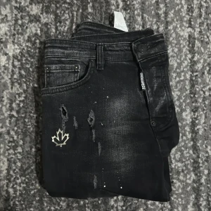 Svarta Dsquared2 jeans med slitningar - Snygga svarta jeans från Dsquared2 med slitna detaljer, blekta partier och coolt löv-märke framtill. Jeansen har smal passform och klassisk femficksdesign. Perfekta för dig som gillar streetstyle och vill sticka ut lite extra. ÄKTA