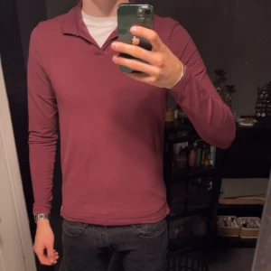 Vinröd pikétröja från Riley - Säljer en vinröd långärmad pikétröja från Riley. Tröjan har klassisk krage utan knappar och är tillverkad i mjuk bomull med lite stretch för extra komfort. Perfekt för dig som gillar stilren och enkel design. 8,5/10