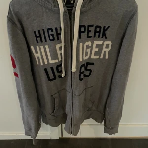 Grå zip hoodie Tommy Hilfiger  - Grå zip hoodie från Tommy Hilfiger i storlek M, modellen är ca 180cm. OBS! flera slitningar finns på tröjan. Hör av dig vid funderingar!