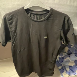 Svart t-shirt från Lacoste - Svart t-shirt från Lacoste med klassisk rund hals och den ikoniska krokodilloggan broderad på bröstet. Enkel och stilren design, perfekt för en clean look. Tillverkad i mjuk bomull för skön komfort.