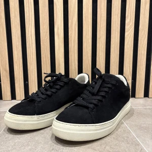 Svarta sneakers Selected Homme stl 42 - Stilrena svarta sneakers från Selected Homme i mocka med vita, tjocka gummisulor och svarta snören. Klassisk rund tå och låg modell som passar perfekt till jeans eller chinos. Tillverkade i Portugal och har en snygg kontrast mellan svart ovandel och vit sula.