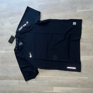 Svart Nike Dri-Fit t-shirt XL/XXL - Svart Nike Dri-Fit t-shirt med reflekterande Swoosh-logga och texten 'Just Do It' på ärmen. Tillverkad i lätt och snabbtorkande material, perfekt för träning. Storleken är XXL, men passar som en XL. Finns att hämta utanför Karlstad annars går frakt att lösa.