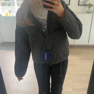 Quiltad svart jacka från WARMWOOD - Quiltad svart jacka från WARMWOOD lik den populära Zara jackan, med dragkedja framtill, två stora fickor och snörning i nederkant. Jackan har en loose passform och är perfekt för dig som gillar en chill och trendig stil. Materialet känns mjukt och jackan är lätt vadderad för extra komfort.