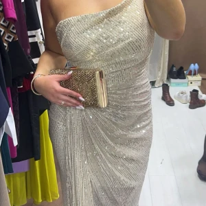 Balklänning/Festklänning i färgen silver - Fin lång balklänning i färgen silver. Har använts endast en gång förut. Den har fina paletter som glittrar i ljuset. Klänningen är lite svagt champagnefärgat men lutar sig mer åt det silvriga hållet. 