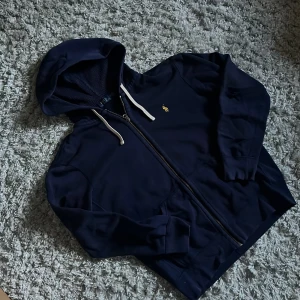 Ralph Lauren Hoodie - Säljer denna snygga Ralph Lauren zip hoodien. Den är marinblå och är i ok skick. Tyvärr har den ett hål på armbågen samt några fläckar som kanske går bort i tvätten. Bara att skriva över frågor och funderingar.