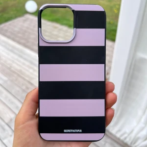 Mobilskal randigt - Ett randigt mobilskal i svart och rosa. Hårdplast. Använts typ 2 gånger 🥰 Passar till iPhone 13 Pro Max.  Längd: 16 cm Bredd: 8 cm