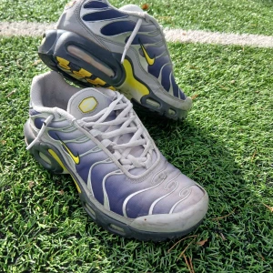 Nike sneakers blå/gul strl 38 - Nike sneakers i blått och grått med gula detaljer och vit snörning. Snygg vågig design på ovandelen och synlig dämpning i sulan. Ikonisk Swoosh-logga i gult på sidan. Ovandel i syntet och mesh för bra andningsförmåga. Perfekt för dig som gillar sportig stil.